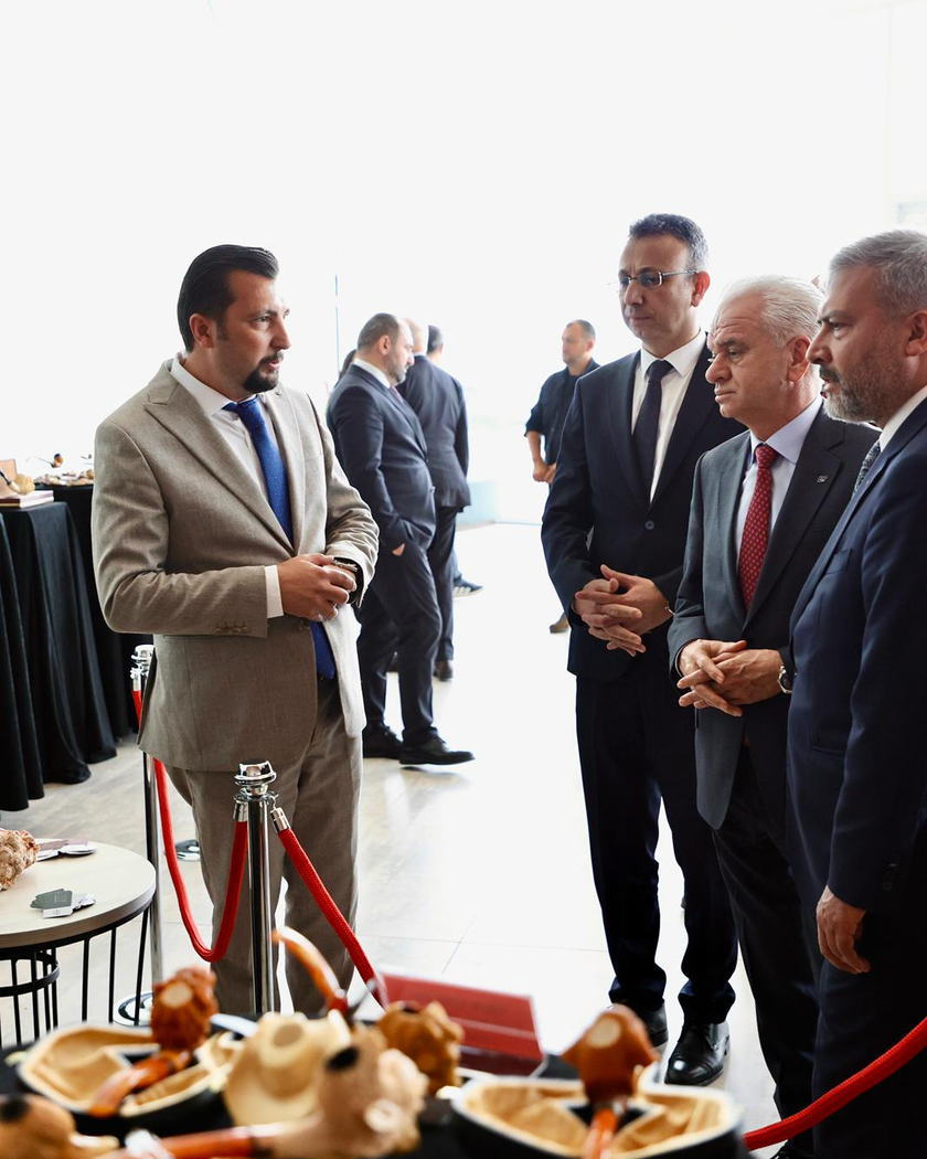 Önde odak dışında kalan lületaşı eserleri, arkada sergi alanında ayakta duran bir grup ziyaretçi.